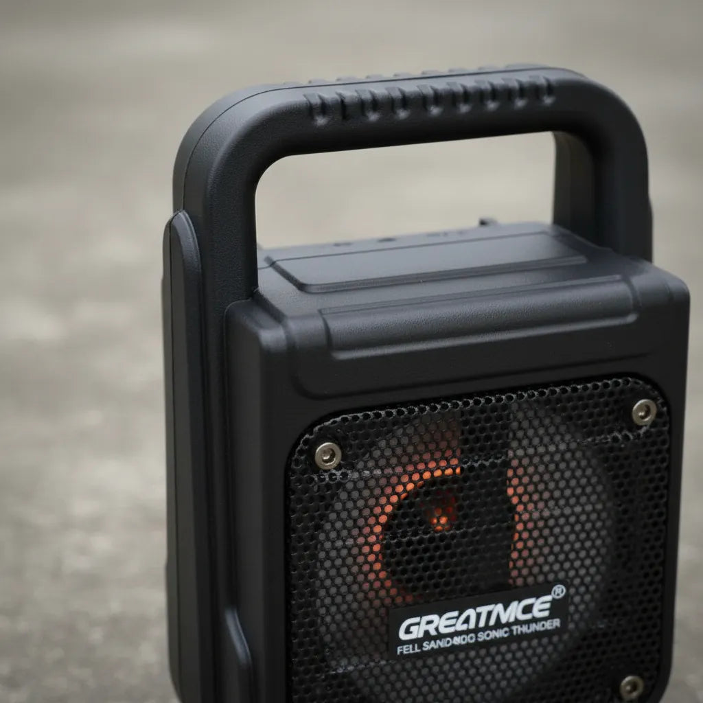 Black portable speaker with handle on a concrete surface, featuring the brand 'GREATMICE'.