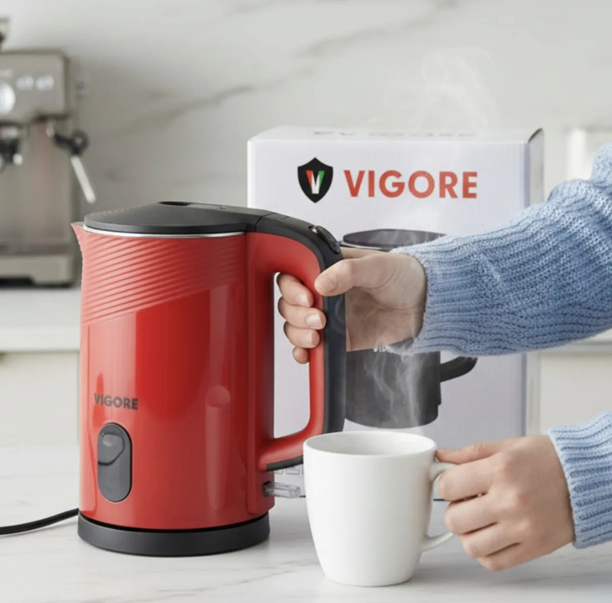 Red VIGORE electric kettle being used to fill a white mug with steam, in front of a branded box.